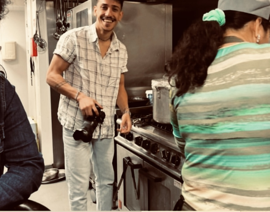 Yousif Amshwaali stands with camera in the Kind Economy kitchen