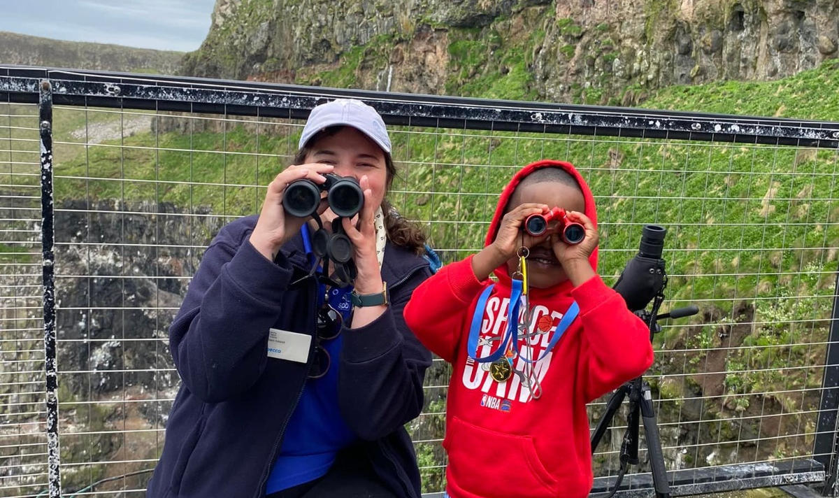 Child and adult both look into binoculars on a bridge on Rathlin island